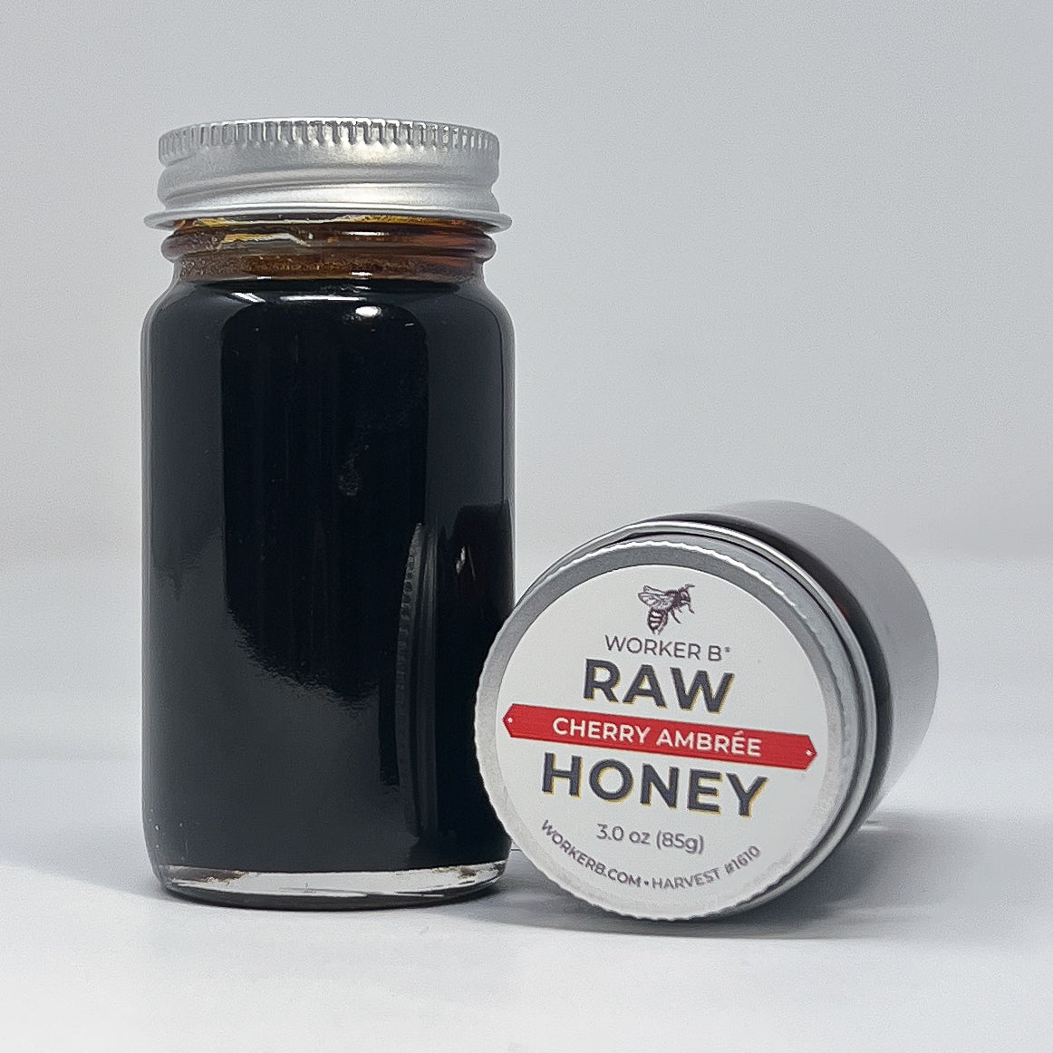 Jar of Worker B Raw Cherry Ambère Honey with label on a white background
