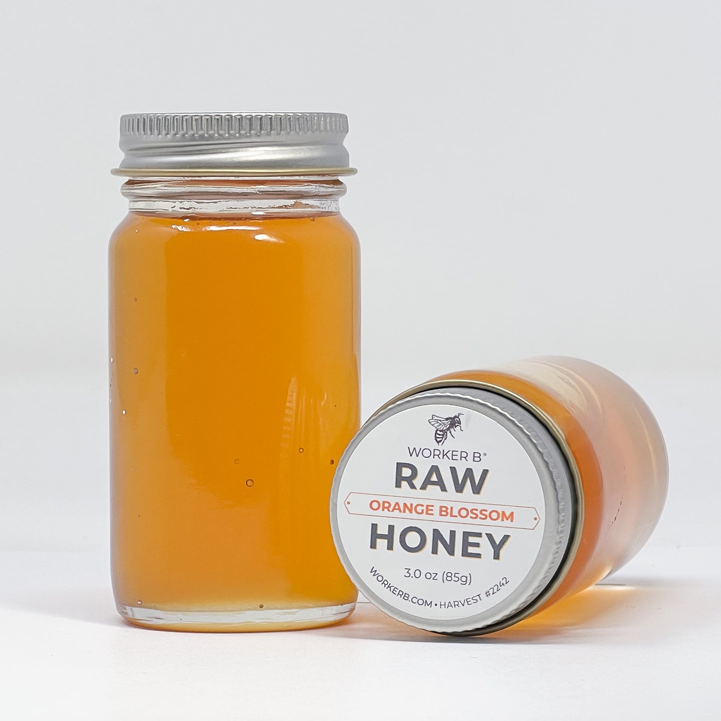 Jar of Worker B Raw Orange Blossom Honey with a white label on a light gray background