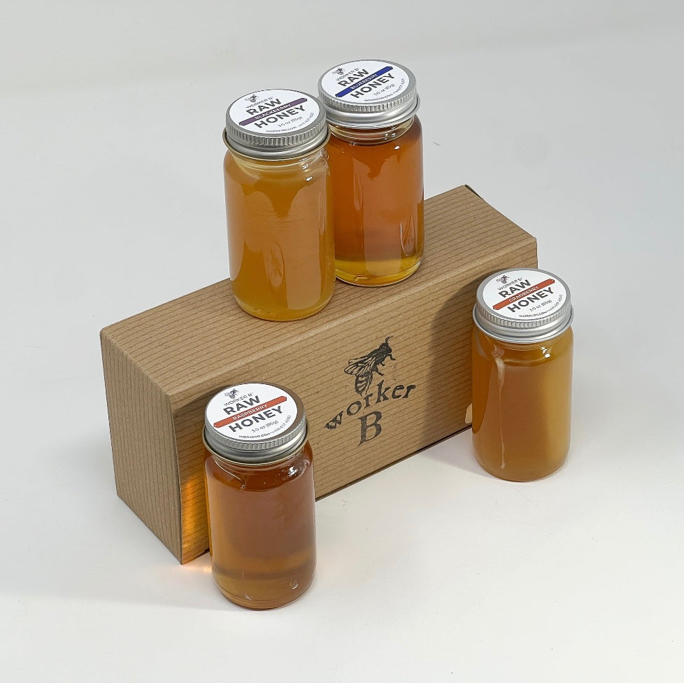 Four jars of raw honey on a wooden stand with 'Worker B' branding.