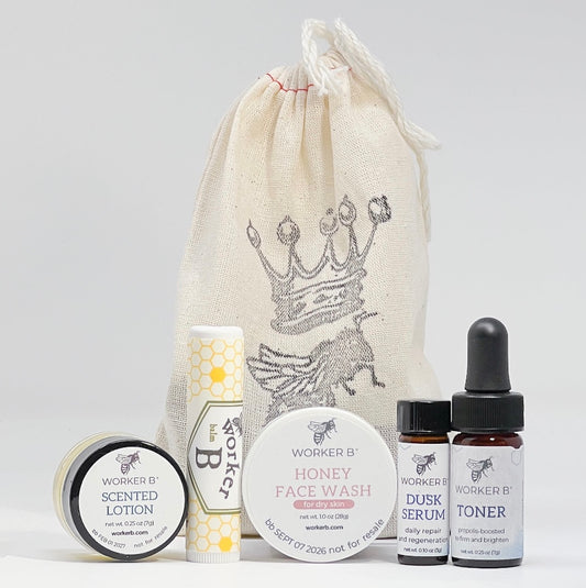 Set of Worker B skincare products including lotion, face wash, serum, and toner with a branded drawstring bag on a light gray background.