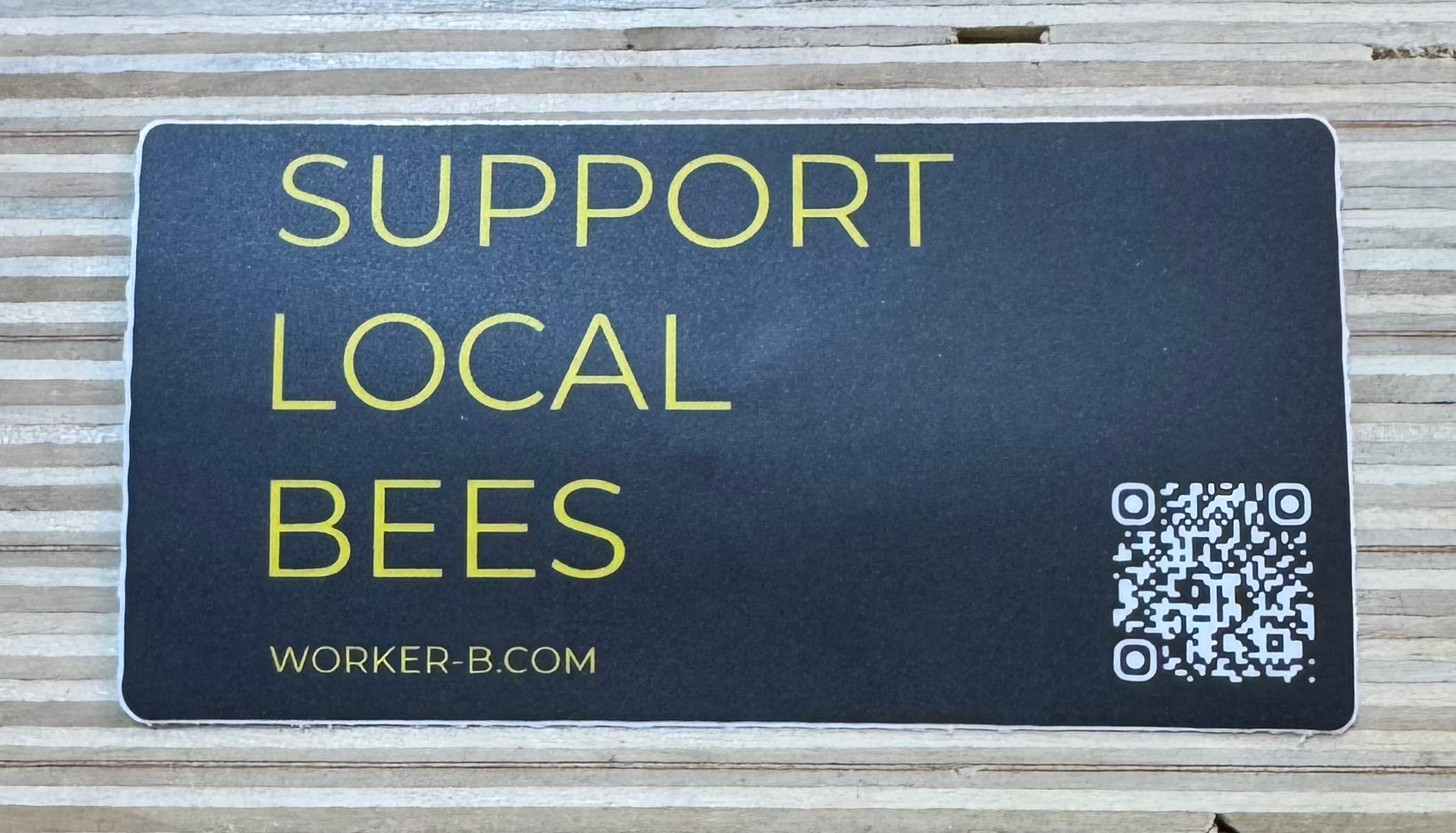 Sticker with 'Support Local Bees' text and QR code on a wooden surface